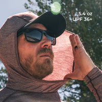 A man outdoors wearing a hooded long-sleeve shirt demonstrating how the fabric blocks the sun
