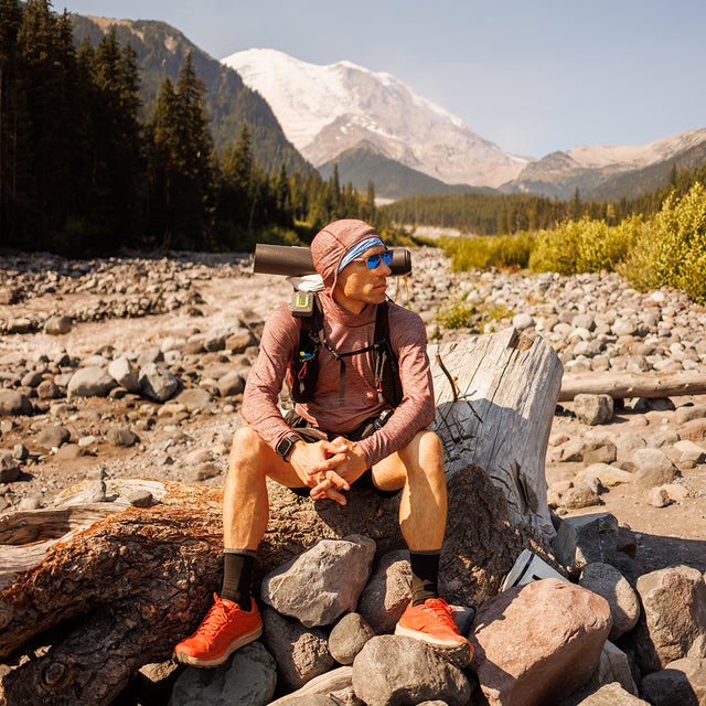 Hiker sitting on a log wearing Outdoor Vitals Tern Ultralight Merino Wool Hoodie.