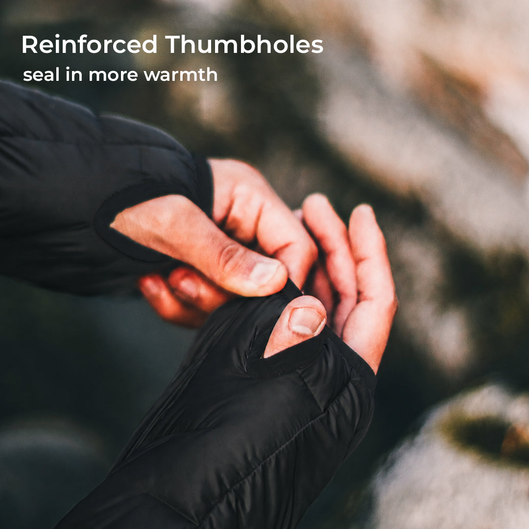 Close-up of a person wearing black fingerless gloves and adjusting the thumbhole opening, with overlaid text reading 'Reinforced Thumbholes' and 'seal in more warmth' against a blurred outdoor rocky background.