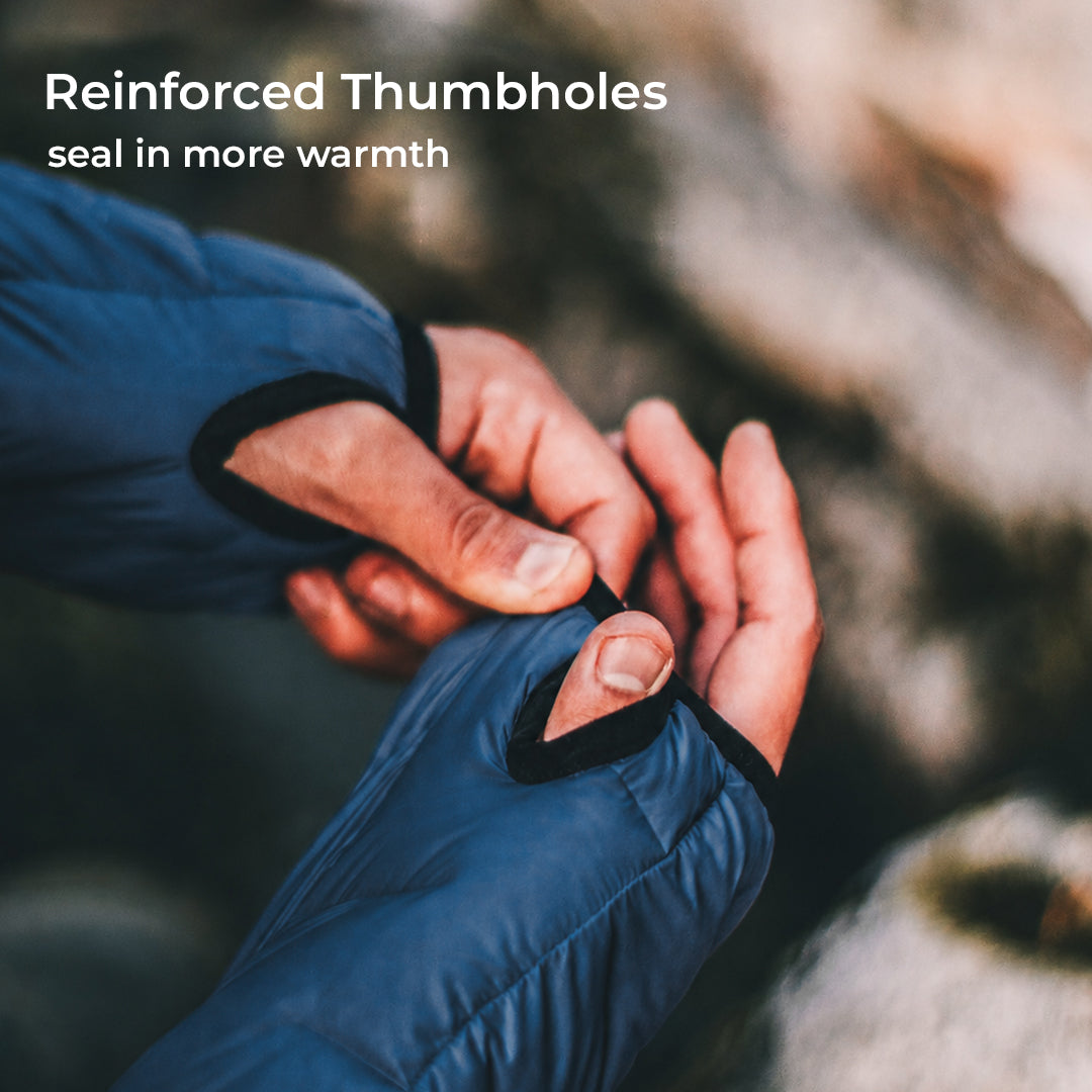 Close-up of a person wearing a blue puffer glove with thumbhole opening and black reinforced trim, adjusting the thumb area. White text at the top reads 'Reinforced Thumbholes' and 'seal in more warmth.