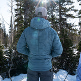 Man wearing insulated hooded down jacket shown from the back in snowy forest setting.