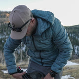 Man wearing insulated down jacket while packing backpacking gear outdoors.