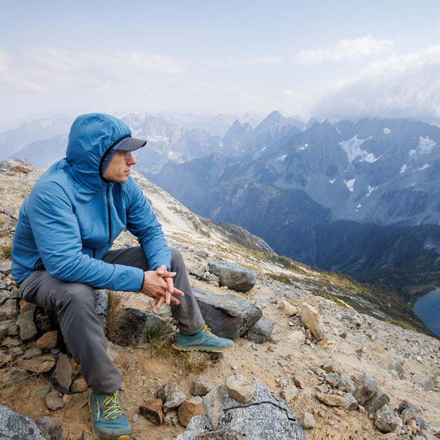 Hiker wearing the Outdoor Vitals Vario Jacket with the hood up on a rocky mountain overlook