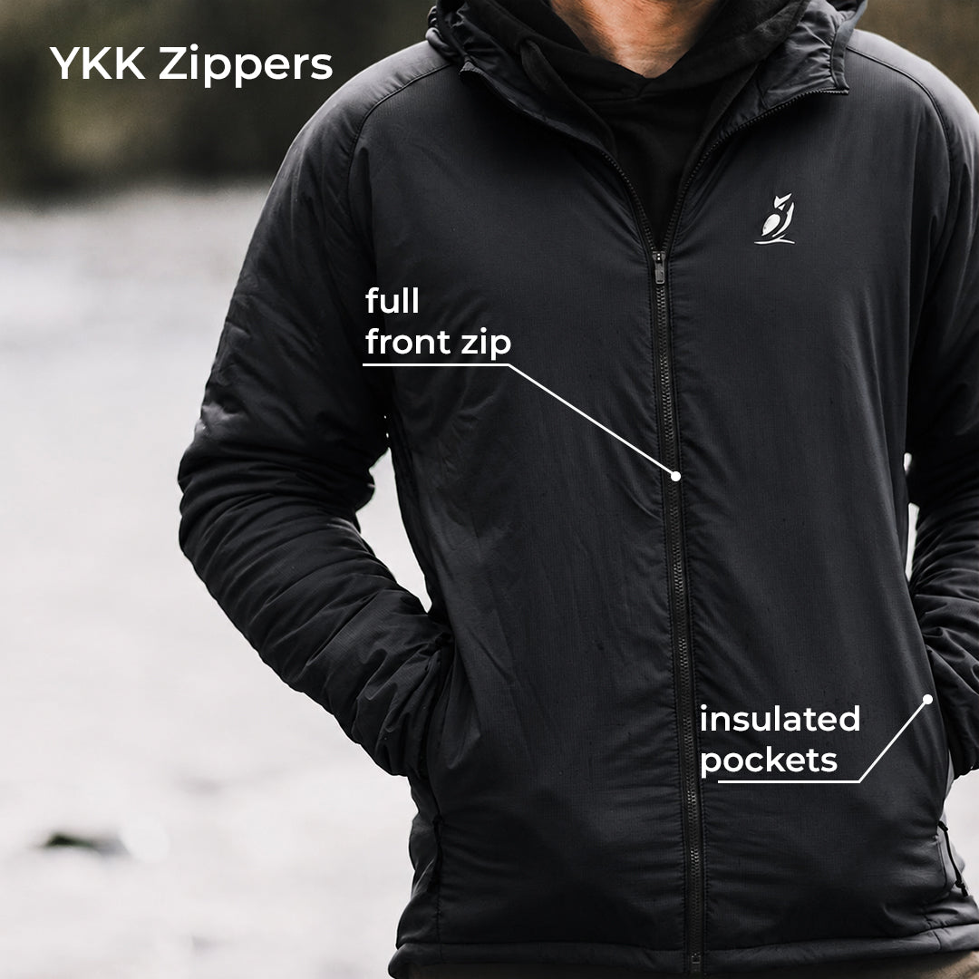 A man wearing a black YKK zippers lightweight jacket, with white text callouts pointing to the 'full front zip' and 'insulated pockets' on a blurred outdoor background.