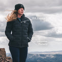 A woman wearing a black puffer jacket and beanie stands outdoors on a rocky mountain ridge under a cloudy sky. White text callouts point to the jacket features: 'YKK Zippers' near the chest and 'Insulated Pockets' near the lower front.