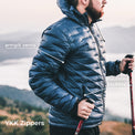 A man wearing a dark blue quilted puffer jacket outdoors on a mountain, with text callouts pointing to armpit vents, insulated pockets, and YKK zippers.