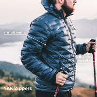 A man wearing a dark blue quilted puffer jacket outdoors on a mountain, with text callouts pointing to armpit vents, insulated pockets, and YKK zippers.