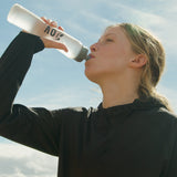side view of woman wearing windbreaker jacket while drinking water from bottle