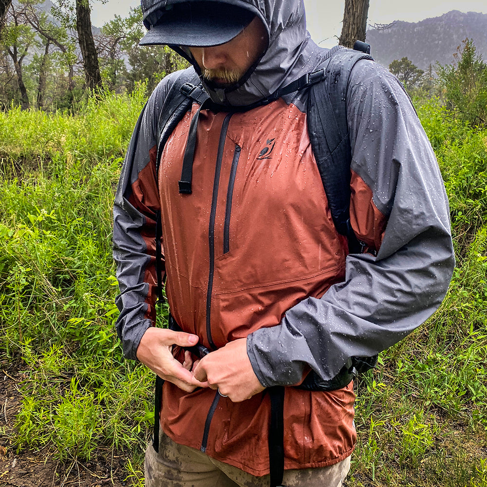 front view as man buckles backpack hip belt over rain jacket during rain storm
